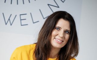 A woman with dark hair smiles in a yellow sweatshirt.